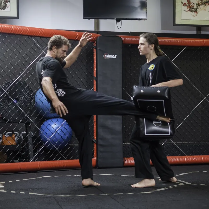 Head Instructor Grant Mundy landing a side kick into a body shield held by a student in the cage